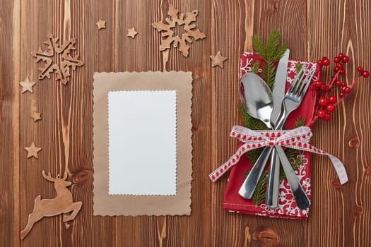 Spoon, knife and fork on red napkin with fir tree branch on a wooden background. Top view with copy space for adding your content. Menu. Advertising