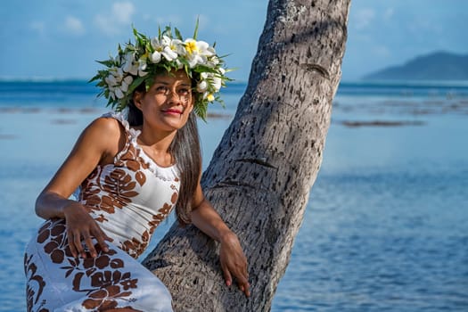 Young woman with flower wreath from Frangipani leans against palm trunk,Raiatea,French Polynesia