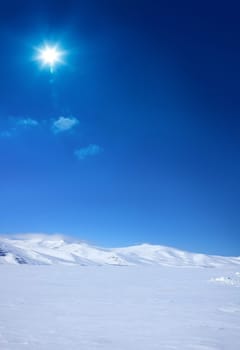 Snow covered empty frozen landscape of mountainside over blue sky with sunbeam