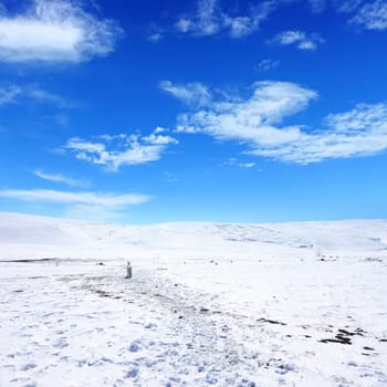 Snow covered empty frozen landscape of mountainside over blue sky with clouds