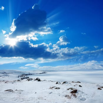 Snow covered empty frozen landscape of mountainside over blue sky with clouds