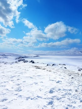 Snow covered empty frozen landscape of mountainside over blue sky with clouds