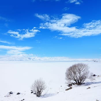 Snow covered empty frozen landscape of mountainside over blue sky with clouds
