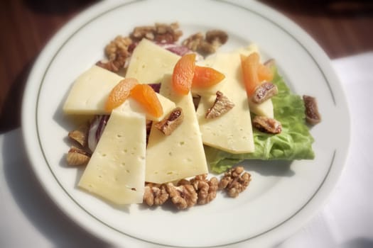 close up plate of cheese and dried fruits with walnut on breakfast table