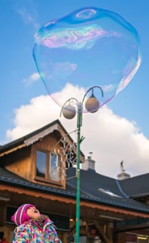 Girl looking at giant soap bubble on the main high street in Karpacz town, polish winter ski resort, Poland