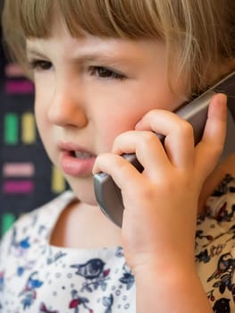 Cute little Caucasian girl talking on the mobile phone while sitting in the train carriage