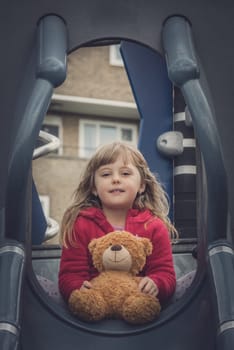 Adorable Caucasian girl holding teddy bear while playing on an outdoor playground