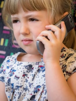 Cute little Caucasian girl talking on the mobile phone while sitting in the train carriage