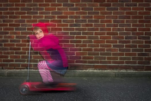 Little Caucasian girl riding fast on her scooter on a road outside her house