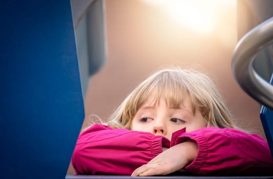 Little young Caucasian girl resting on the top of the big outdoor slide on a playground