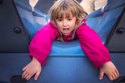 Little young Caucasian holding on to the small holes to prevent from sliding backwards down the big outdoor slide on a playground