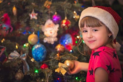 Cute happy and smiling Caucasian Christmas girl putting the decorations on the Christmas tree