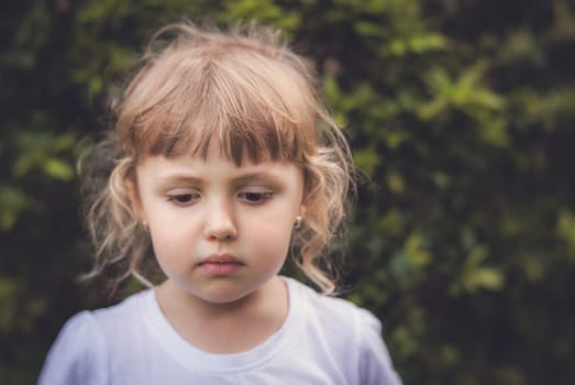 Portrait of a little sad Caucasian girl in a garden in summer