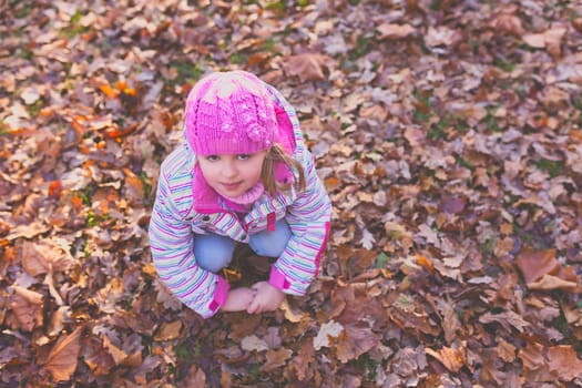 Portrait of a cute girl wearing pink hat resting on the ground full of autumn leaves