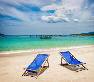 Beautiful white sand beach. Chairs on foreground, fishing boats on background. Landscape of Vietnam