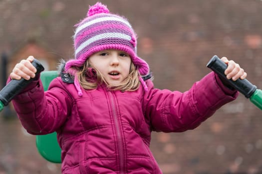 Little Caucasian girl exercising on the outdoor training machine on a chilly autumn day