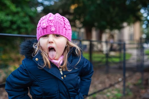 Cute naughty Caucasian girl wearing pink hat sticking her tongue out