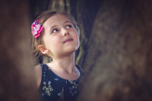 Portrait of a cute Caucasian girl playing hide and seek in a dark forest in summer