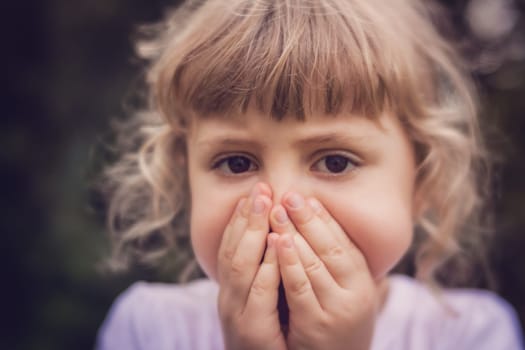 Little girl standing in the park with her hands covering her mouth indicating she is scared or worried