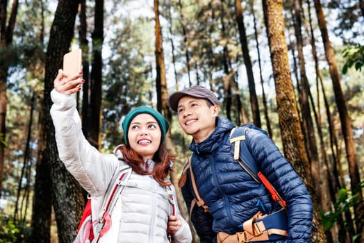 Attractive asian hikers couple taking selfie photo with mobile phone on the forest