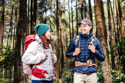 Young asian hikers couple with backpack standing and looking each other in the forest.