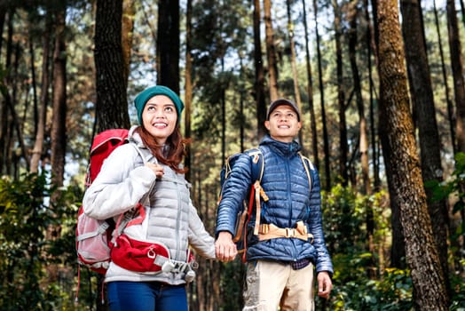 Happy asian hikers couple with backpack walking while holding hands on the forest