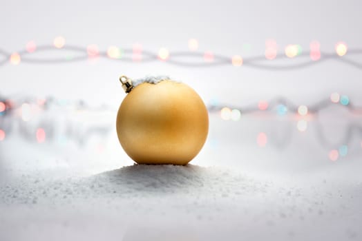 Yellow christmas ball on snow with blurred lights background. Christmas decoration