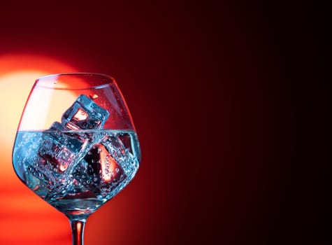 Glass of wine with ice cubes against red bright background