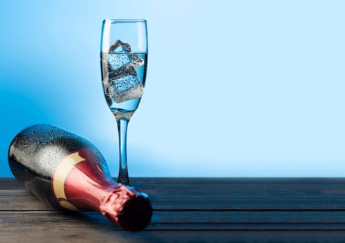 White wine glass with ice cubes and bottle on wooden table