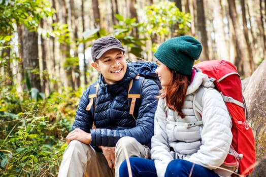 Smiling asian couple hikers with backpack looking at each other on forest