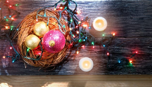 Christmas balls in wooden nest with christmas lights and candles on wooden floor. Christmas ornament
