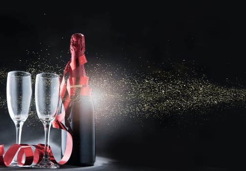 Wine bottle and glasses with red ribbon and golden glitters over black background. New year and celebration concept