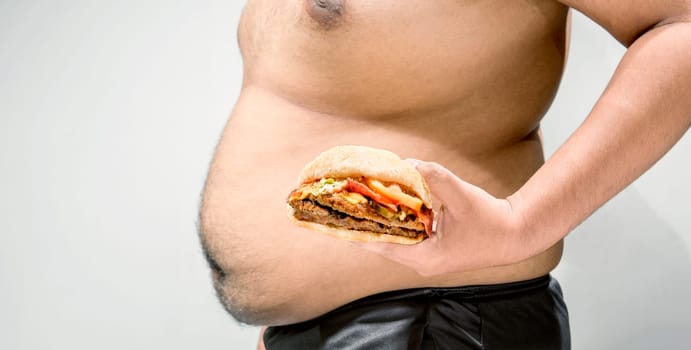 Man with overweight belly holding hamburger on his hand over white background