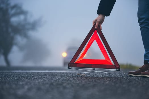Traffic problem in thick fog. Driver putting warning triangle behind his broken car.