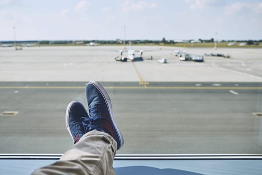 Man waiting at airport. Personal perspective of traveler from window to taxiways and runway.