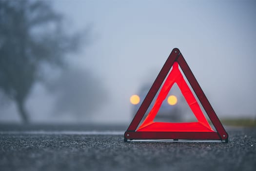 Traffic problem in thick fog. Car on the road behind warning triangle.