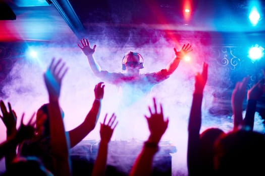 Male deejay in headphones and sunglasses looking at dancing crowd