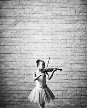 Little girl in tutu playing the violin against brick wall