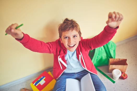 Ecstatic schoolboy with raised arms sitting by the wall