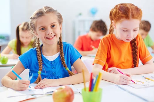 Pretty pupil drawing at lesson with her friend near by