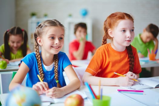 Happy little girl sitting at lesson with her friend near by