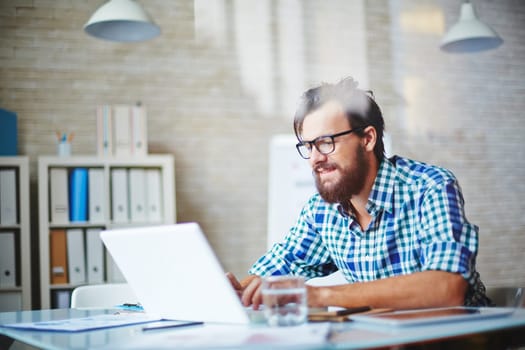 Handsome young businessman in casualwear networking on laptop