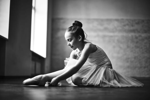 Cute little ballerina in tutu tying up her shoes