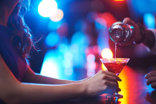 Young woman holding martini glass while barman pouring cocktail