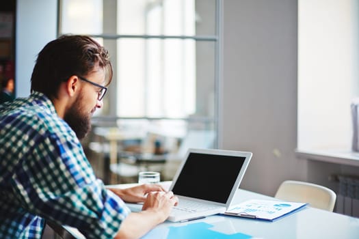 Modern businessman sitting at workplace and typing