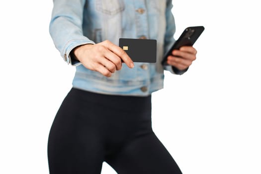 woman in denim holding mobile phone and black premium credit bank card on white background. woman paying with plastic credit card on smartphone app,