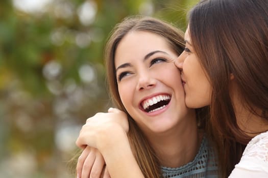 Woman laughing with perfect teeth while a friend is kissing her with a green background