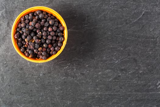Bowl of juniper berries on stone surface with copy space.