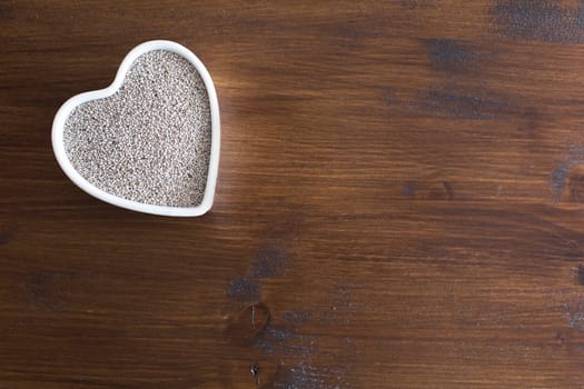 White Chia seeds in heart shaped container on table with copy space