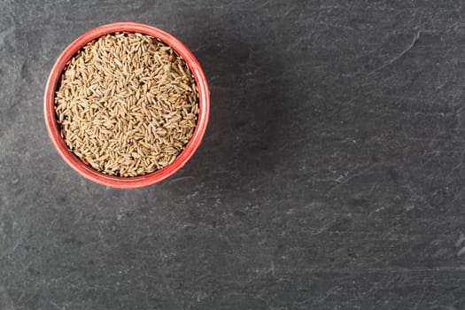 Bowl of caraway seeds on stone surface with copy space.